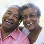 A Black older man and woman smile with their heads together after getting tooth replacements in Petaluma, CA
