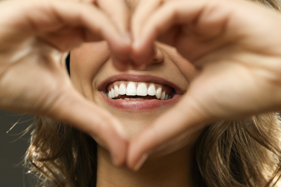 closeup of a woman holding her hands in a heart shape in front of her beautiful smile