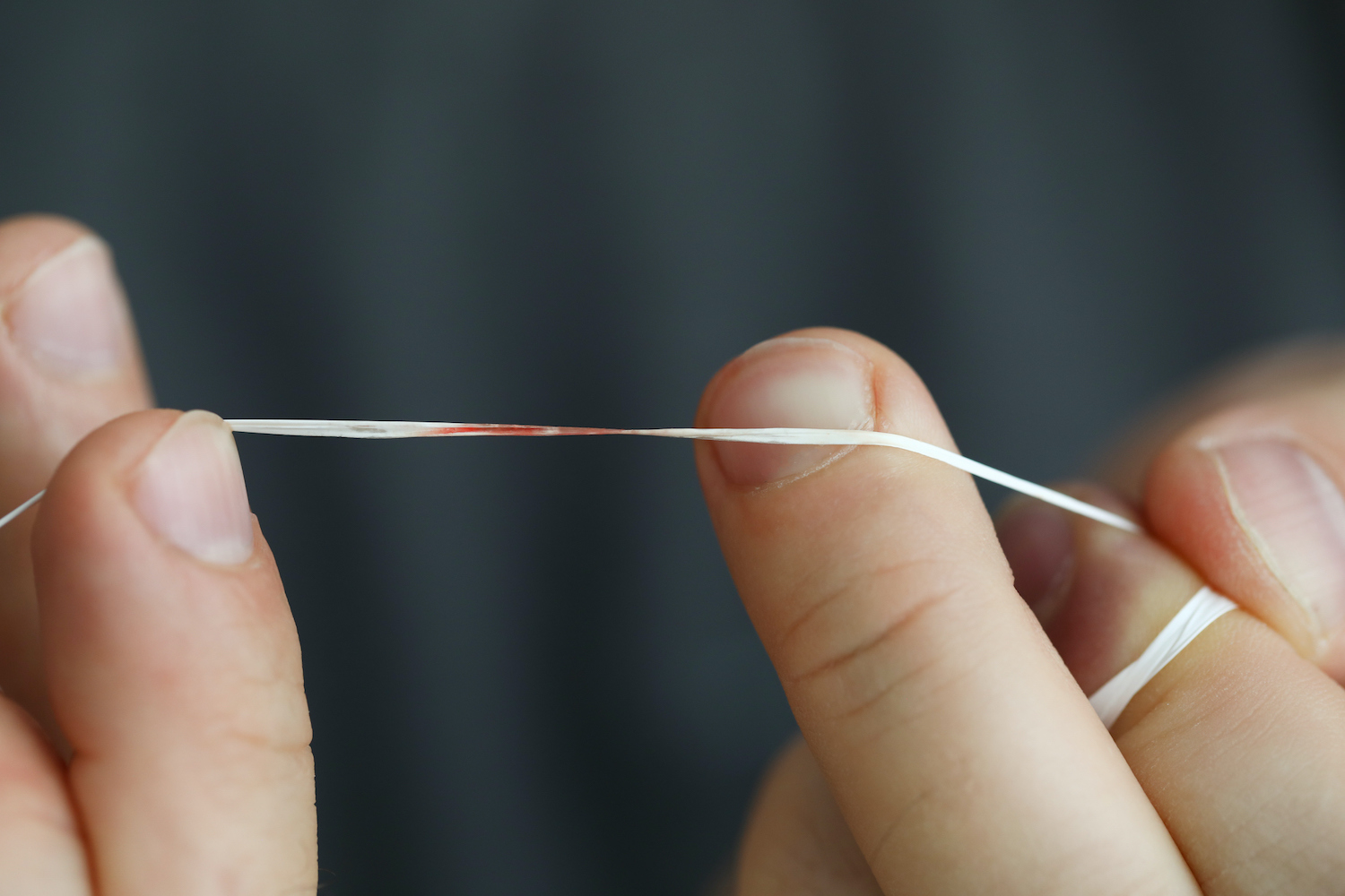 Closeup of fingers holding a string of floss with blood on it