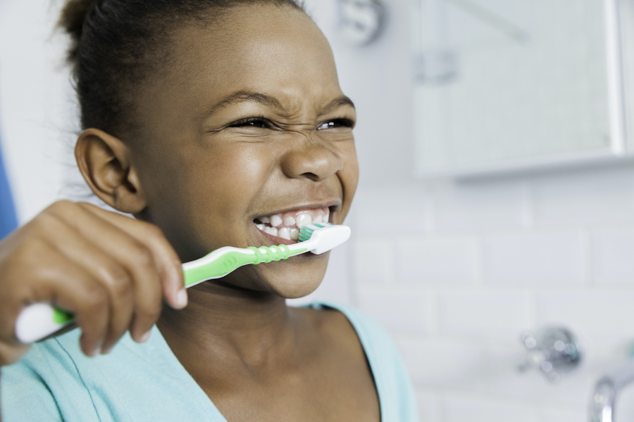 Black young girl smiles as she brushes her teeth with a green toothbrush