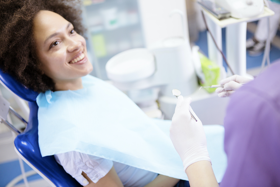 Black woman in a dental chair smiles at her dental hygienist during her dental cleaning appointment