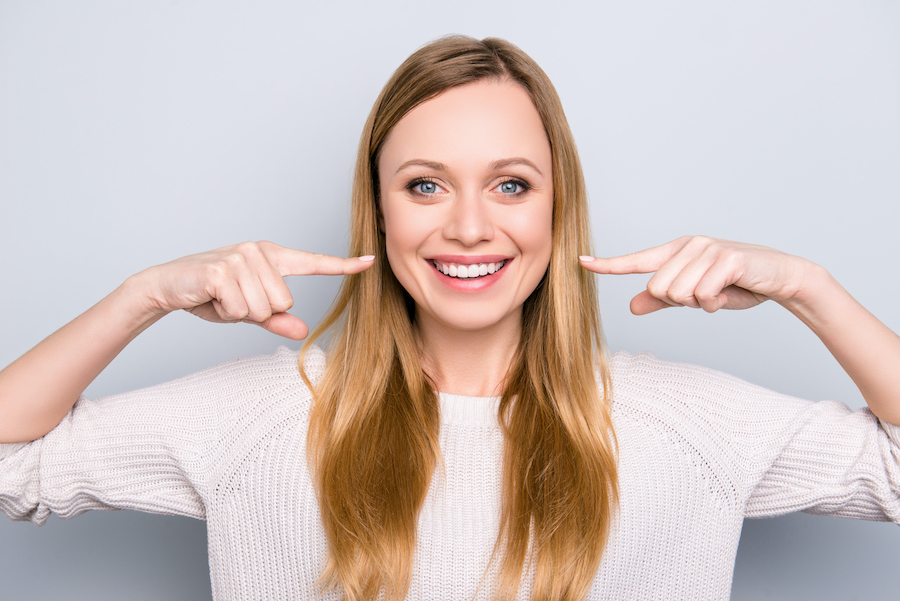 Blonde woman smiles and points to her teeth