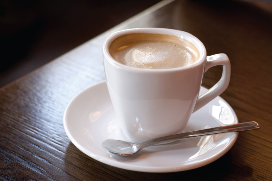 a white mug filled with coffee on a white saucer with a silver spoon on a wooden table