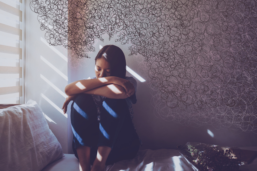 A woman sits with her knees to her chest and her arms on her knees surrounded by squiggly lines to represent stress and anxiety