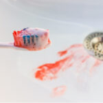 Closeup of a toothbrush with blood on its bristles over a sink with foamy blood near the drain from bleeding gums