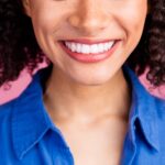 smiling woman in blue shirt on pink background how to get dental veneers to last
